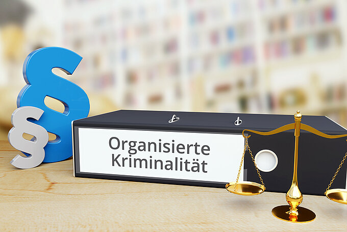 Organisierte Kriminalität – Recht/Gesetz. Ordner auf Schreibtisch mit Beschriftung neben Paragraf und Waage. Anwalt